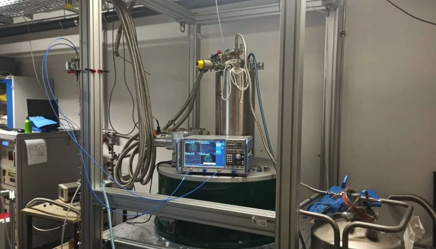 Eine Wissenschaftlerin und ein Wissenschaftler arbeiten hinter einer Glasfassade und mischen Chemikalien mit Großgeräten.