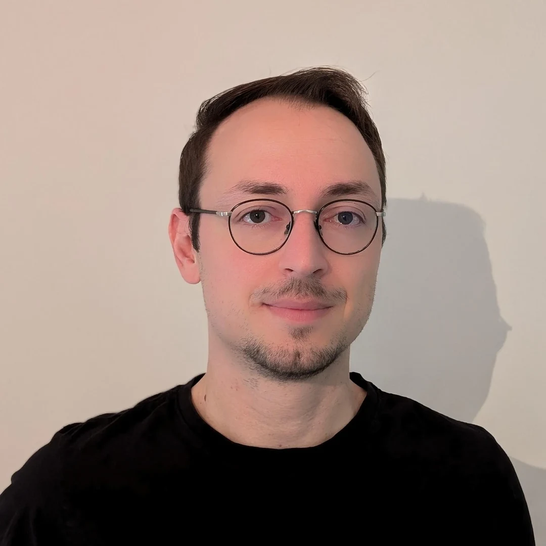 Eine Wissenschaftlerin und ein Wissenschaftler arbeiten hinter einer Glasfassade und mischen Chemikalien mit Großgeräten.